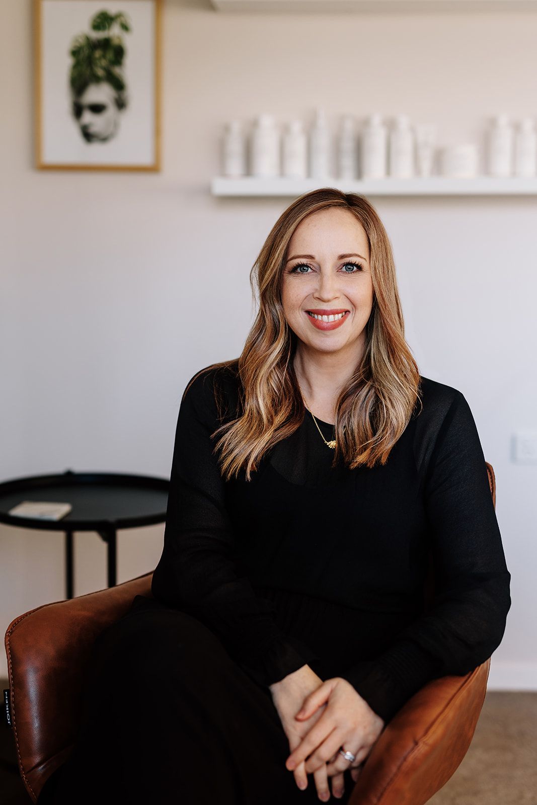 Hayley seated in a leather chair in the studio, calm white-wall background.
