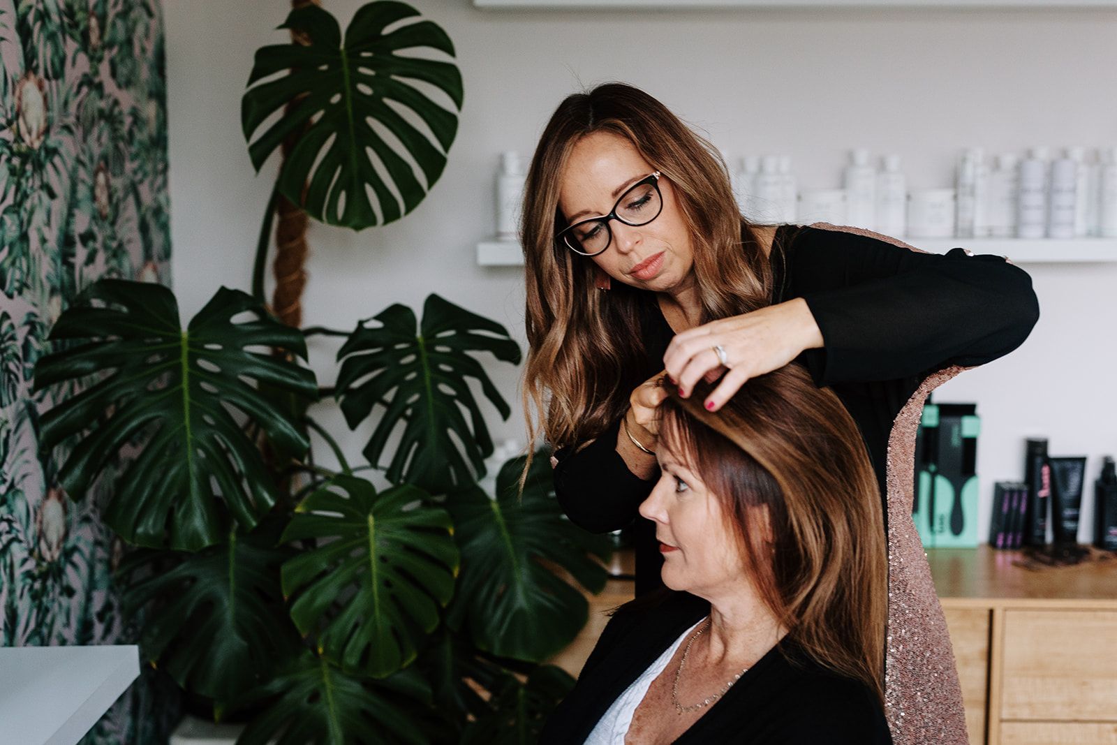 Hayley styling a client beside a monstera plant in the studio.